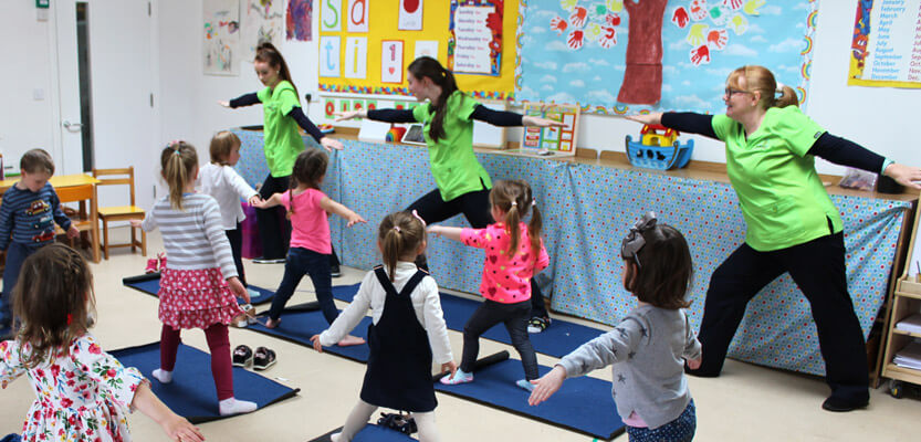three teachers demonstrating yoga poses to class of children